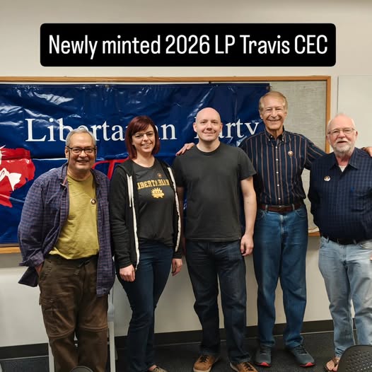 The 2026 LP Travis County Executive Committee standing together in front of a Libertarian Party banner.